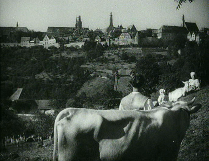 Hans im Glück (D 1936): Die Titelfigur (Erwin Linder) mit Kuh vor imposanter Stadtkulisse / © Icestorm